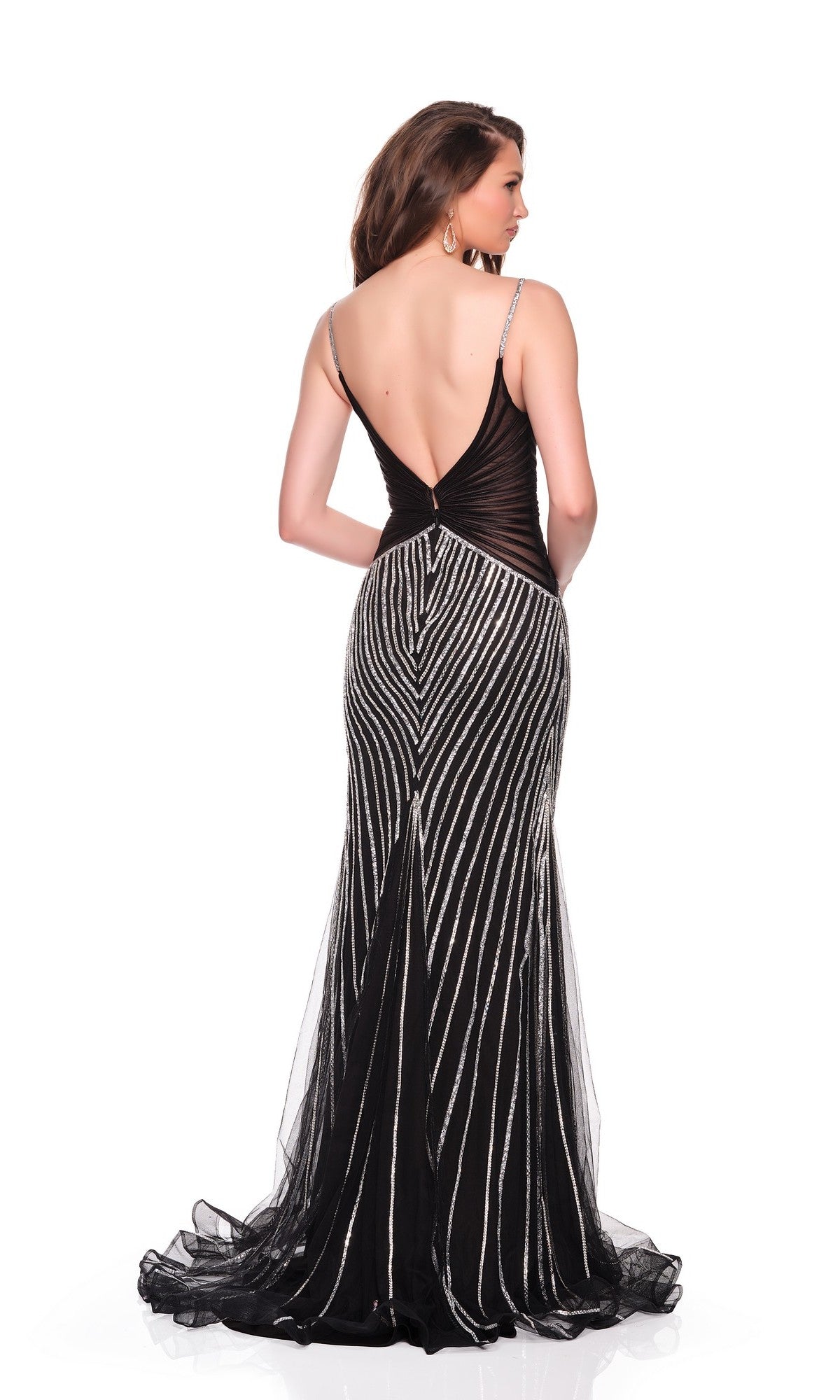 A woman faces away from the camera, modeling the Dave and Johnny 12607 long black fitted prom dress with silver vertical stripes, a deep V-back, and hot-stone embellishments against a white background.